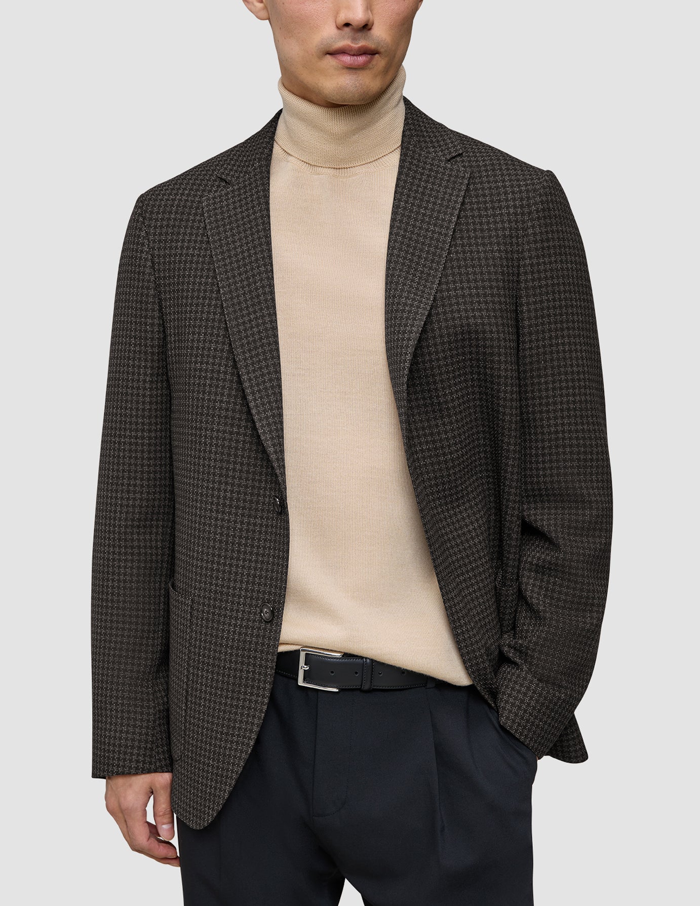 Eine Person, die einen dunkelbraunen, karierten Timeless Wool Blazer Slim über einem beigen Rollkragenpullover und einer schwarzen Hose trägt.